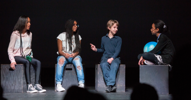 Four students on stage performing a play